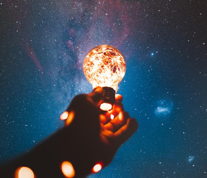 Human arm holding a lit light bulb against a dark sky