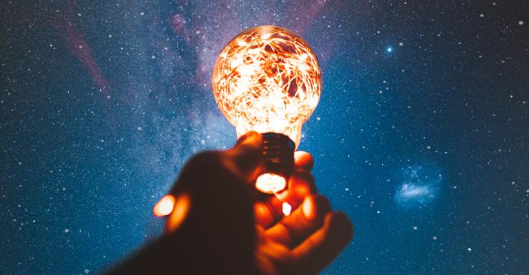 Human arm holding a lit light bulb against a dark sky