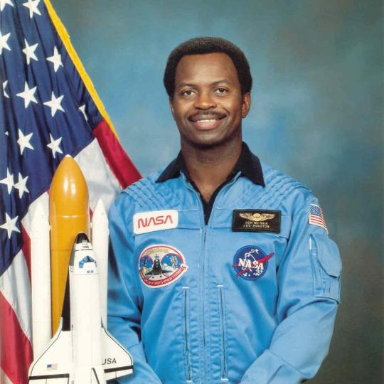 Ronald E. McNair in a NASA uniform sitting next to an American flag